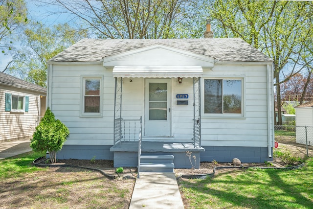 bungalow-style home featuring fence and roof with shingles