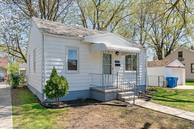 view of front of home featuring roof with shingles, a detached garage, a front lawn, and an outbuilding
