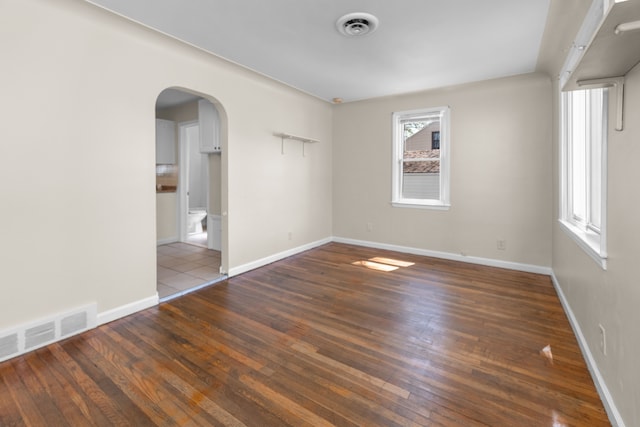 unfurnished bedroom with wood-type flooring, arched walkways, visible vents, and baseboards