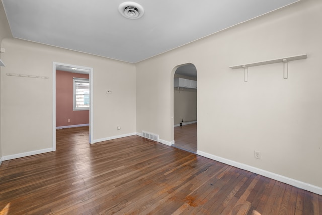 spare room with arched walkways, visible vents, hardwood / wood-style flooring, and baseboards