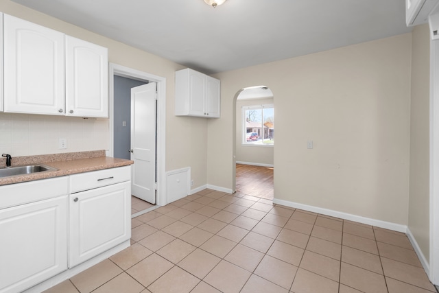 kitchen featuring light tile patterned floors, white cabinets, a sink, light countertops, and arched walkways