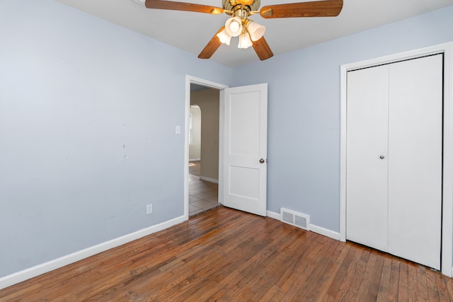 unfurnished bedroom featuring hardwood / wood-style floors, a closet, baseboards, visible vents, and a ceiling fan