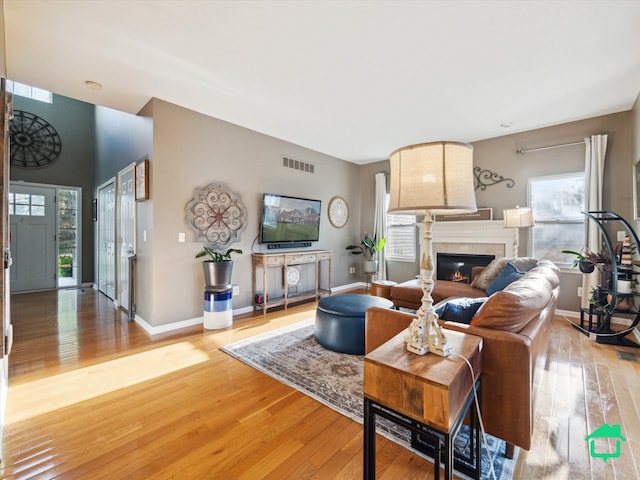 living area with a glass covered fireplace, light wood-style floors, visible vents, and baseboards