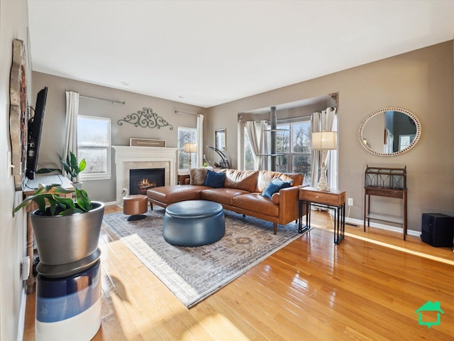 living area with baseboards, wood finished floors, a wealth of natural light, and a lit fireplace