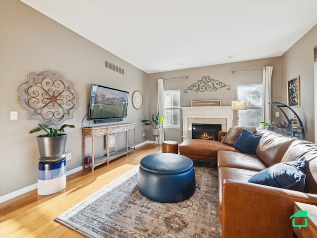 living room with visible vents, baseboards, wood finished floors, and a glass covered fireplace
