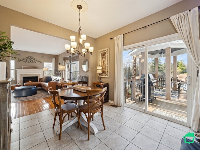 dining space with a warm lit fireplace, light tile patterned flooring, an inviting chandelier, and plenty of natural light