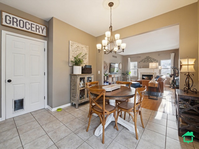 dining room with light tile patterned floors, baseboards, a chandelier, and a glass covered fireplace