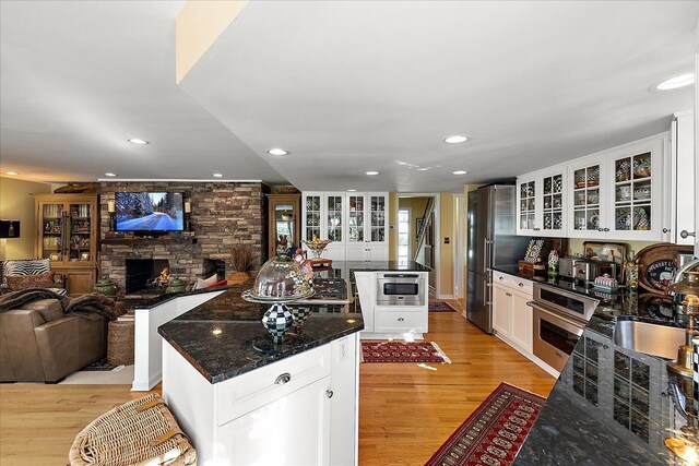 kitchen with white cabinets, appliances with stainless steel finishes, light wood-style floors, a stone fireplace, and a center island