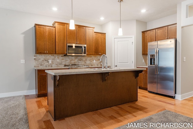 kitchen featuring a kitchen breakfast bar, a sink, stainless steel appliances, brown cabinetry, and backsplash
