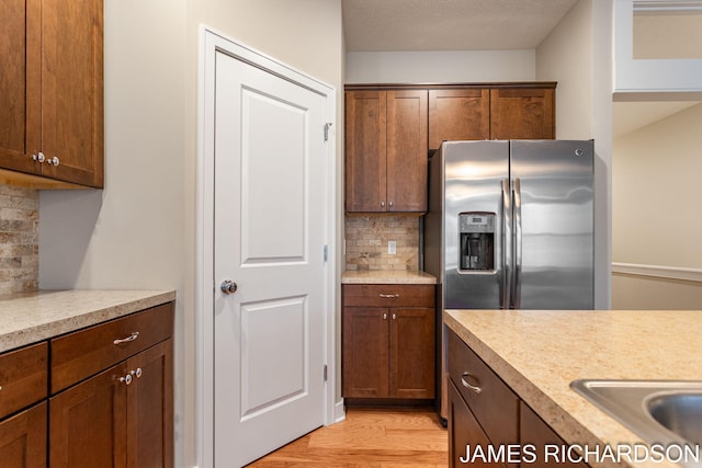 kitchen with decorative backsplash, stainless steel fridge, light wood-style floors, light countertops, and a sink