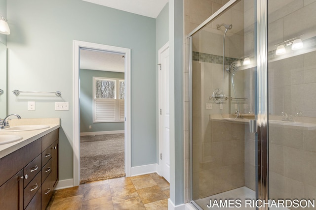 bathroom featuring baseboards, a stall shower, double vanity, and a sink