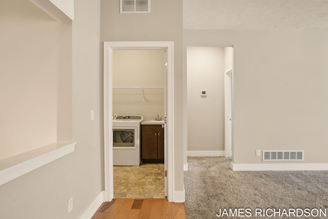 corridor featuring baseboards, visible vents, washer / dryer, and a sink