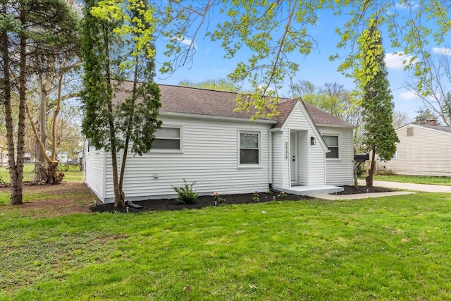 back of house with a lawn and roof with shingles