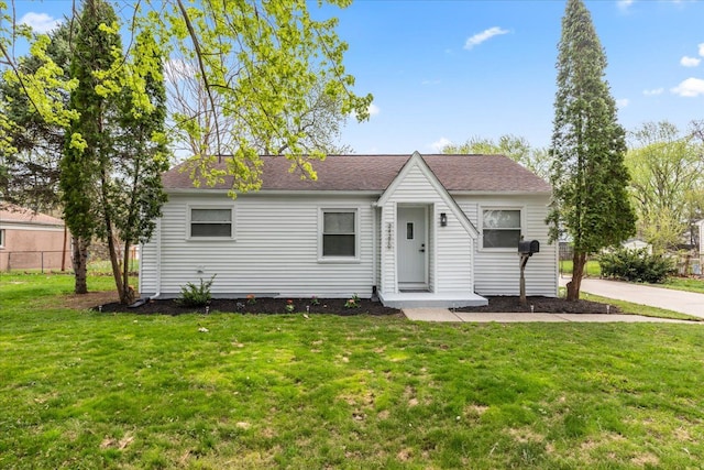 view of front of property featuring fence, roof with shingles, and a front yard