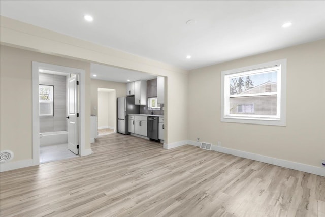 unfurnished living room with baseboards, visible vents, a sink, and light wood-style floors