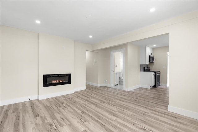 unfurnished living room featuring a glass covered fireplace, baseboards, and light wood-type flooring