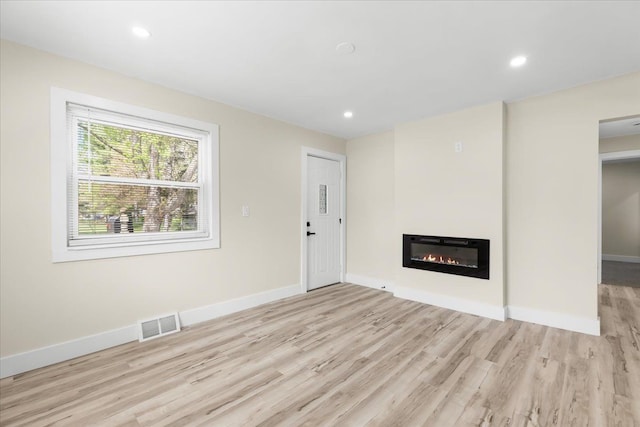 unfurnished living room featuring a glass covered fireplace, baseboards, wood finished floors, and visible vents