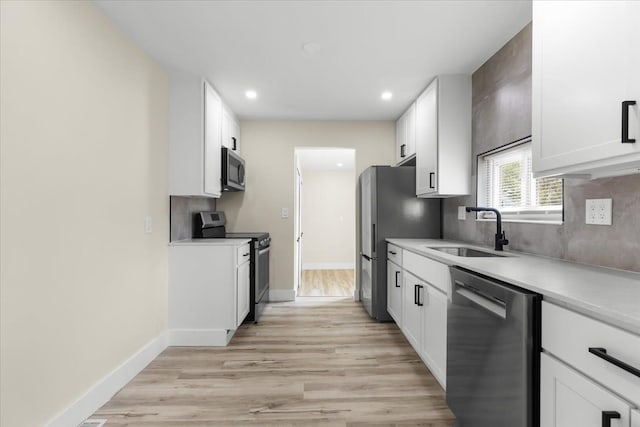 kitchen featuring white cabinets, a sink, light countertops, stainless steel appliances, and light wood-type flooring