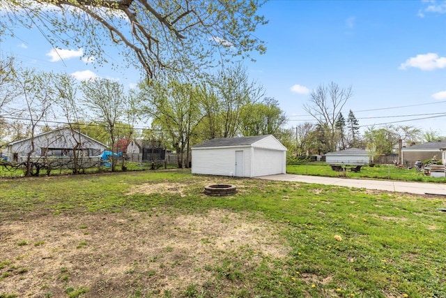 view of yard with a detached garage, fence, a fire pit, and an outdoor structure
