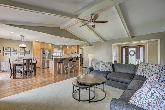 living room with plenty of natural light, vaulted ceiling with beams, ceiling fan with notable chandelier, and visible vents