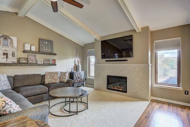 living room with visible vents, wood finished floors, vaulted ceiling with beams, a tiled fireplace, and a ceiling fan