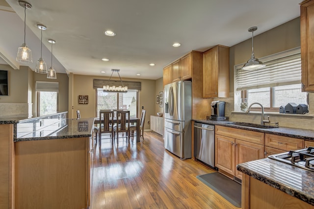 kitchen featuring decorative backsplash, hanging light fixtures, wood finished floors, a sink, and stainless steel appliances