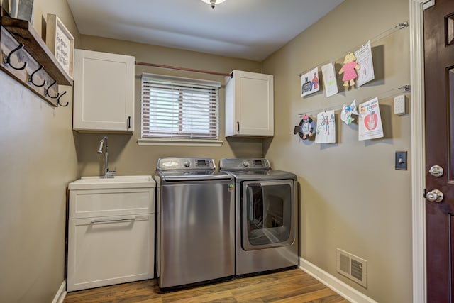 laundry room featuring cabinet space, a sink, separate washer and dryer, wood finished floors, and visible vents