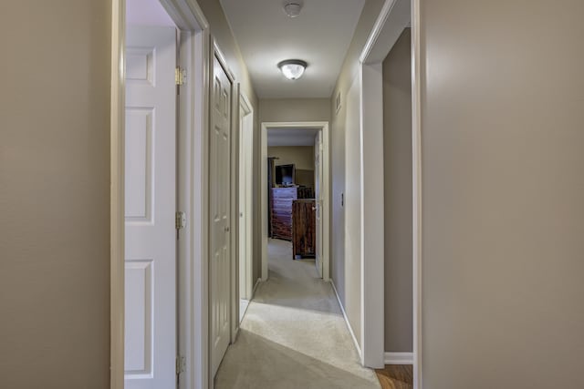 hallway with baseboards and light colored carpet