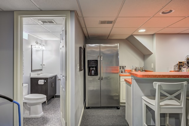 interior space with visible vents, a drop ceiling, indoor bar, stainless steel fridge with ice dispenser, and a sink