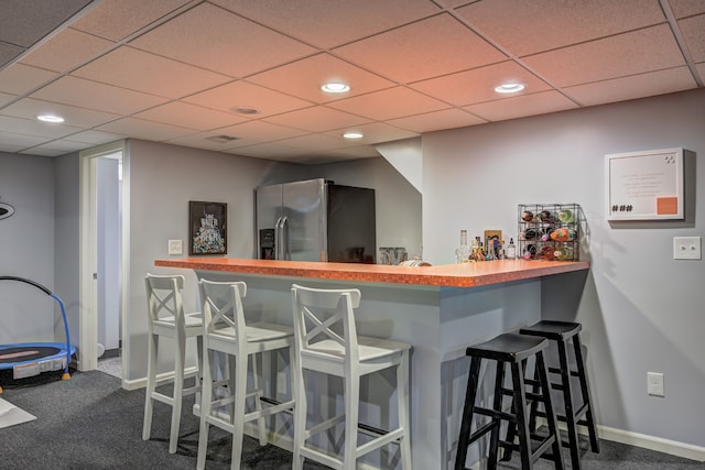 bar with carpet flooring, stainless steel fridge, bar, a paneled ceiling, and baseboards