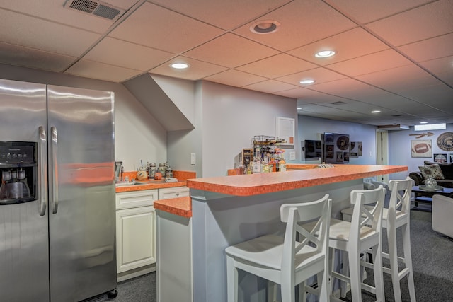 kitchen featuring stainless steel fridge with ice dispenser, a breakfast bar area, a paneled ceiling, dark carpet, and visible vents