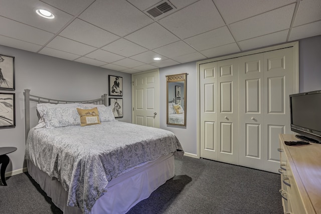 bedroom with baseboards, a closet, dark carpet, and a paneled ceiling