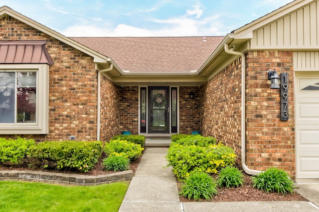 entrance to property with board and batten siding, brick siding, roof with shingles, and a garage