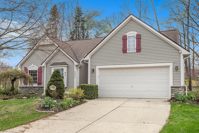 traditional-style house with a shingled roof, a front yard, concrete driveway, and stone siding