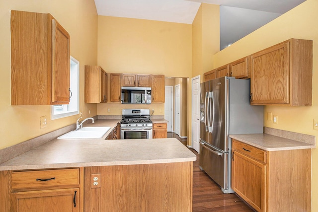 kitchen with a sink, stainless steel appliances, light countertops, dark wood-type flooring, and a peninsula