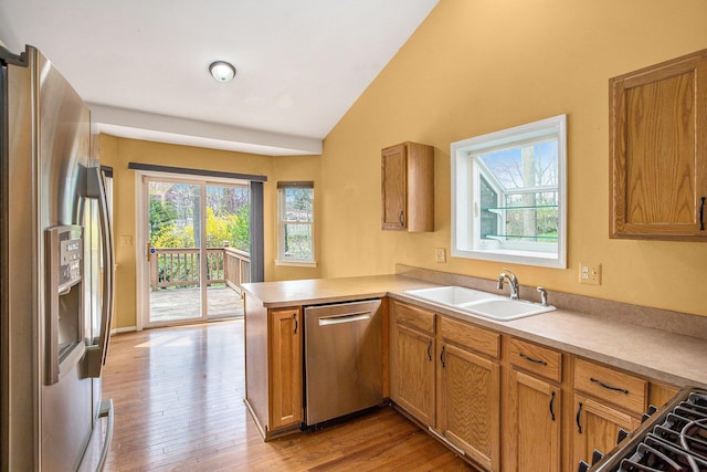 kitchen with lofted ceiling, a sink, light wood-style floors, stainless steel appliances, and a peninsula