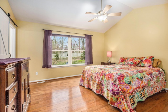 bedroom with visible vents, a barn door, baseboards, light wood-type flooring, and vaulted ceiling