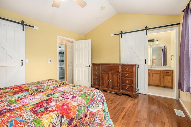 bedroom featuring lofted ceiling, wood finished floors, a barn door, and visible vents