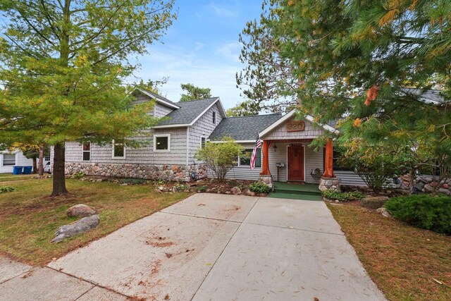 320 Marble St, Cadillac, MI 49601 - view of front of house with a shingled roof, stone siding, a porch, a front yard, and driveway