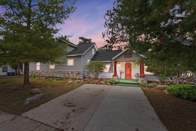 320 Marble St, Cadillac, MI 49601 - view of front of home featuring roof with shingles, covered porch, concrete driveway, and stone siding