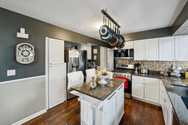 kitchen with appliances with stainless steel finishes, dark wood finished floors, a center island, white cabinetry, and decorative backsplash