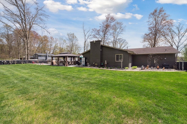 back of property featuring a gazebo, brick siding, a lawn, and a chimney