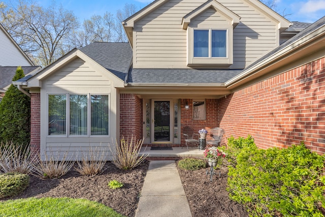 entrance to property with a porch, brick siding, and roof with shingles
