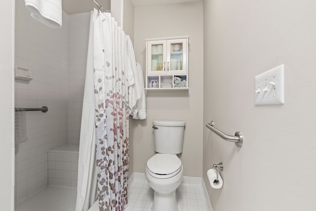 bathroom with toilet, tile patterned floors, a tile shower, and baseboards