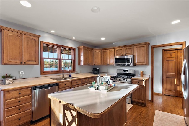 kitchen with appliances with stainless steel finishes, a sink, light countertops, brown cabinetry, and wood finished floors