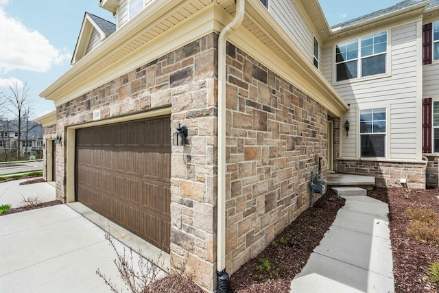 view of side of property featuring stone siding, concrete driveway, and a garage