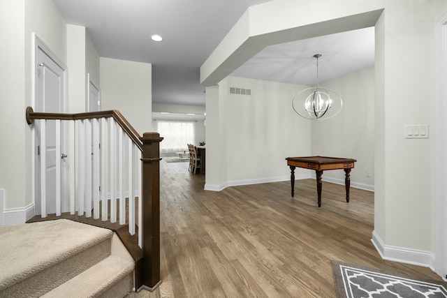 stairs featuring wood finished floors, visible vents, a notable chandelier, and baseboards