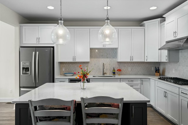 kitchen with a sink, dark wood-style flooring, under cabinet range hood, pendant lighting, and appliances with stainless steel finishes