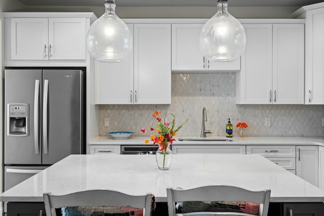 kitchen with stainless steel fridge, hanging light fixtures, a sink, and white cabinets