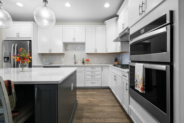 kitchen with under cabinet range hood, appliances with stainless steel finishes, light countertops, and a sink